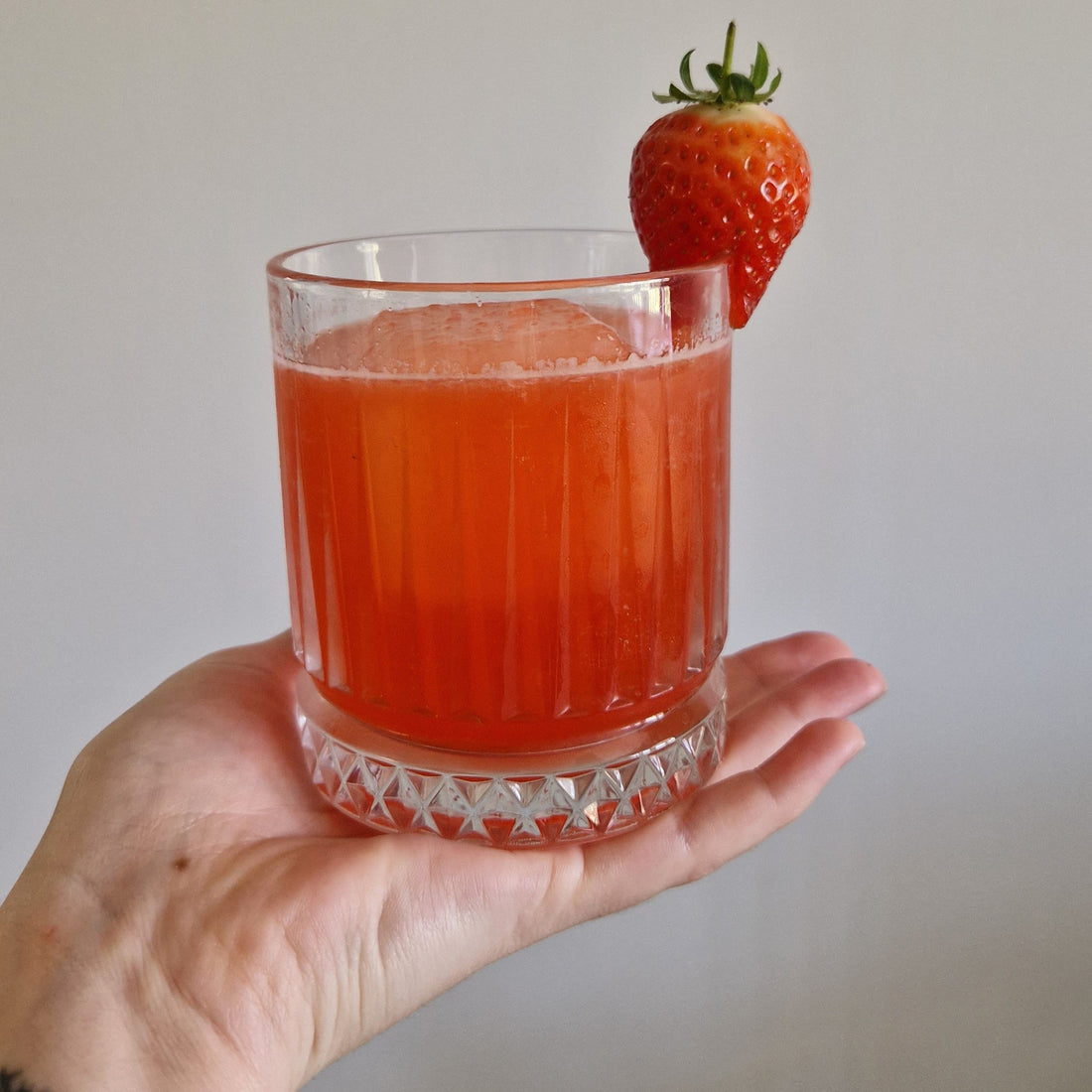 A short glass with iced green tea mixed with fresh strawberries 